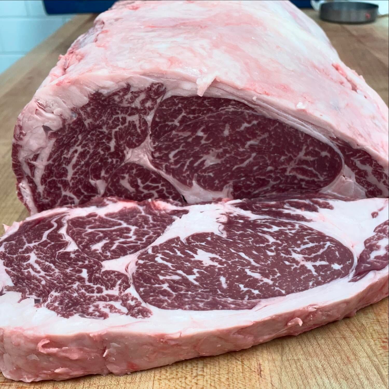 Raw, marbled ribeye steak on a wooden surface, showcasing red and white fat distribution.