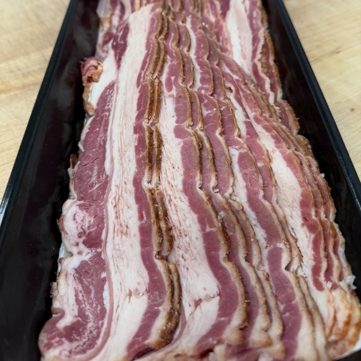 Sliced bacon in a black tray, ready for cooking, with red and white marbling.