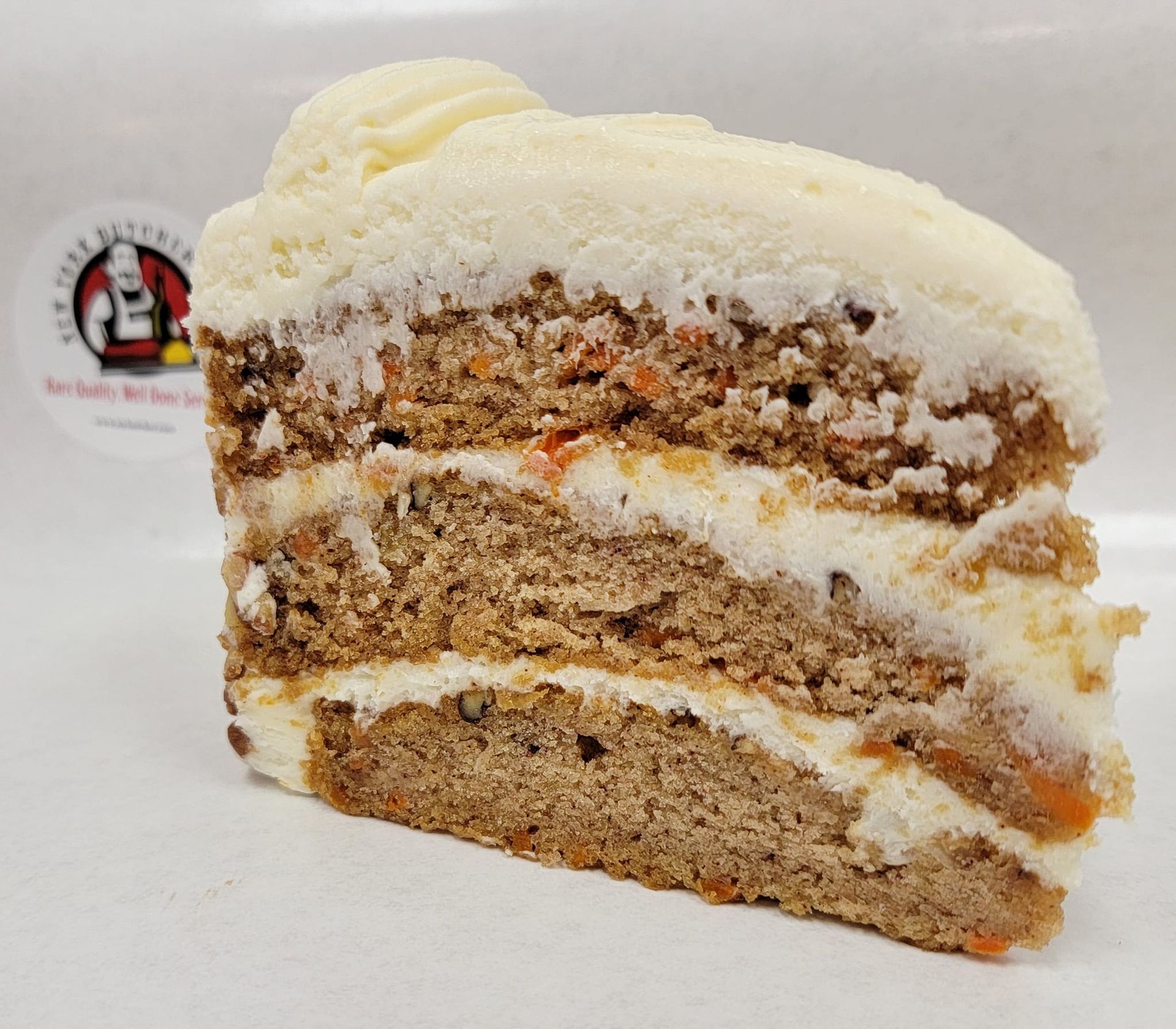 Slice of carrot cake with cream cheese frosting, showing layers of cake and frosting.