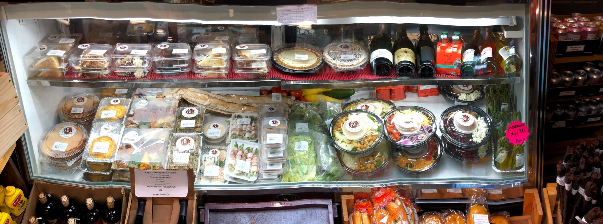A refrigerated display case filled with prepared foods, including salads, cheeses, and packaged goods.
