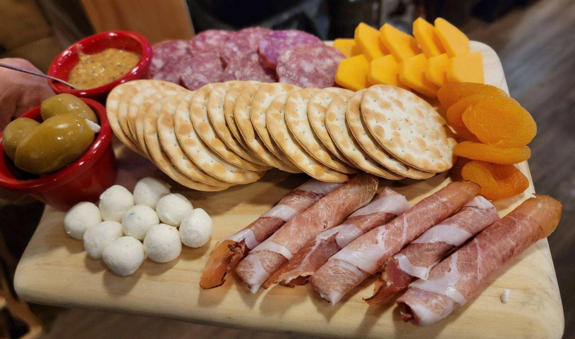 Charcuterie board with meats, cheeses, crackers, olives, quail eggs, and dried apricots.