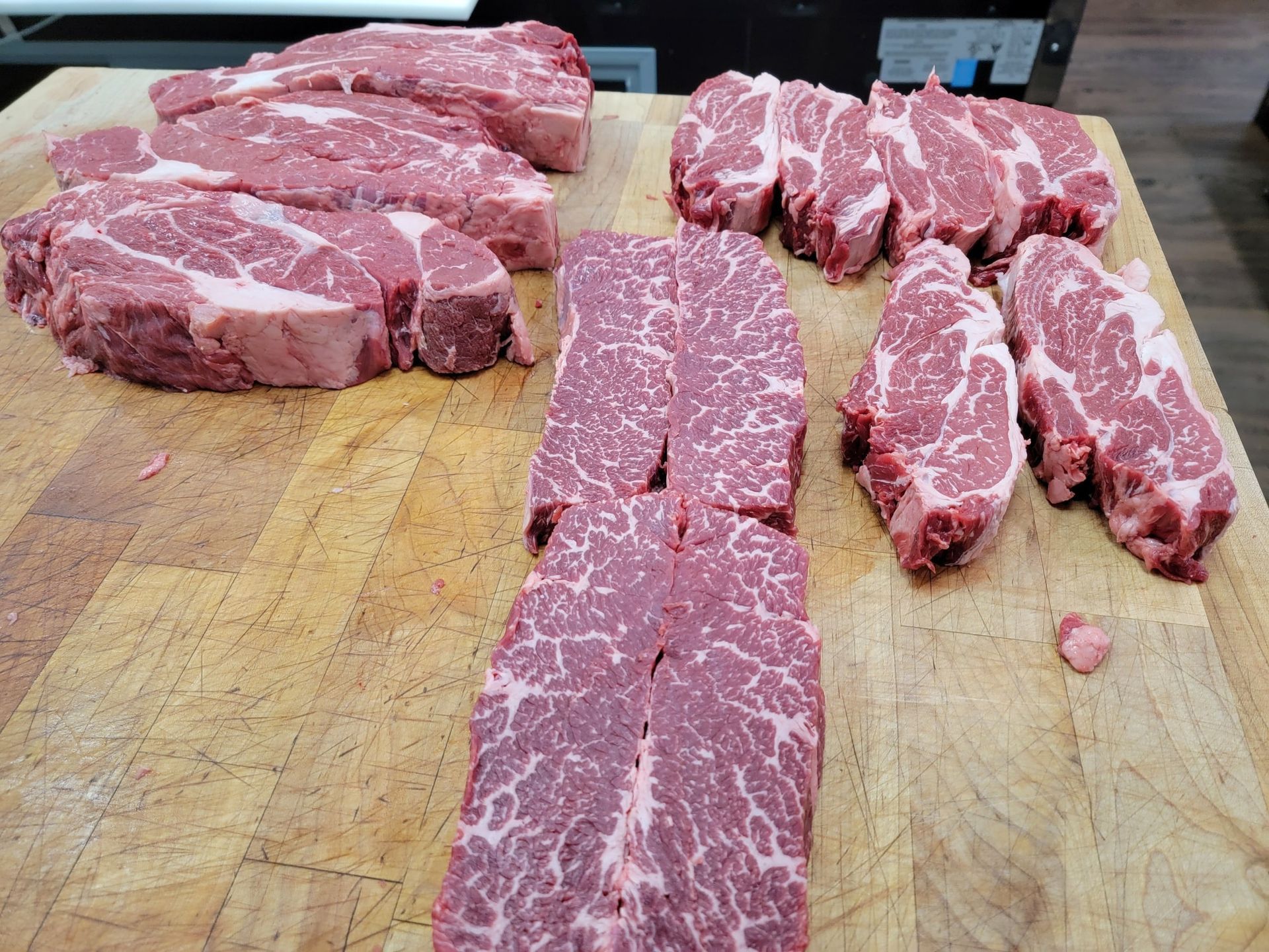 Raw steaks of various cuts arranged on a wooden cutting board.