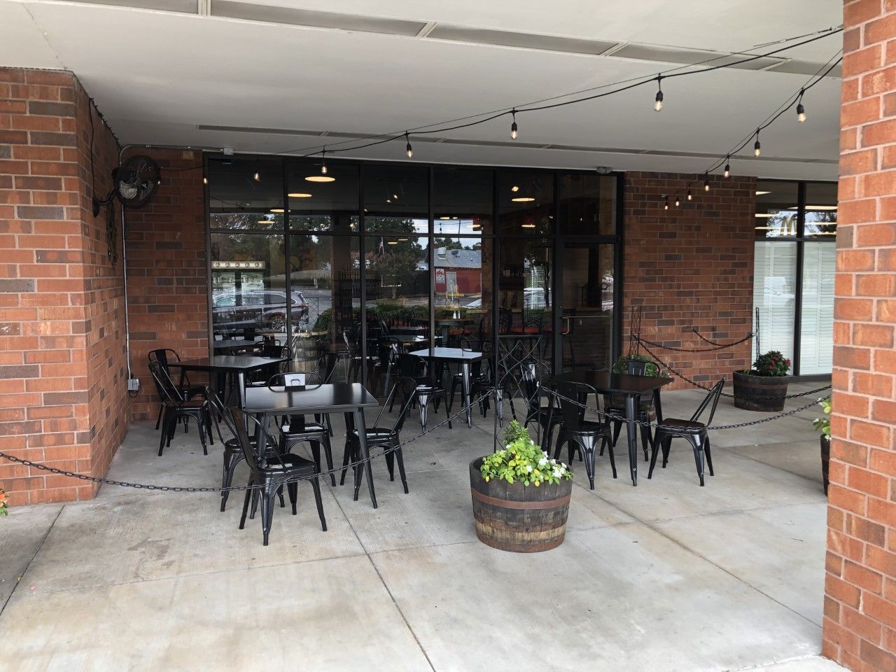 Outdoor seating area with black tables and chairs under a covered patio, red brick building.