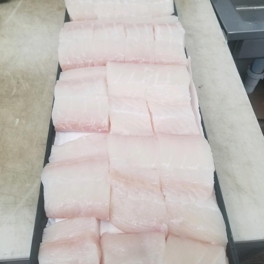 Tray of raw, white fish fillets, neatly sliced and arranged for preparation.