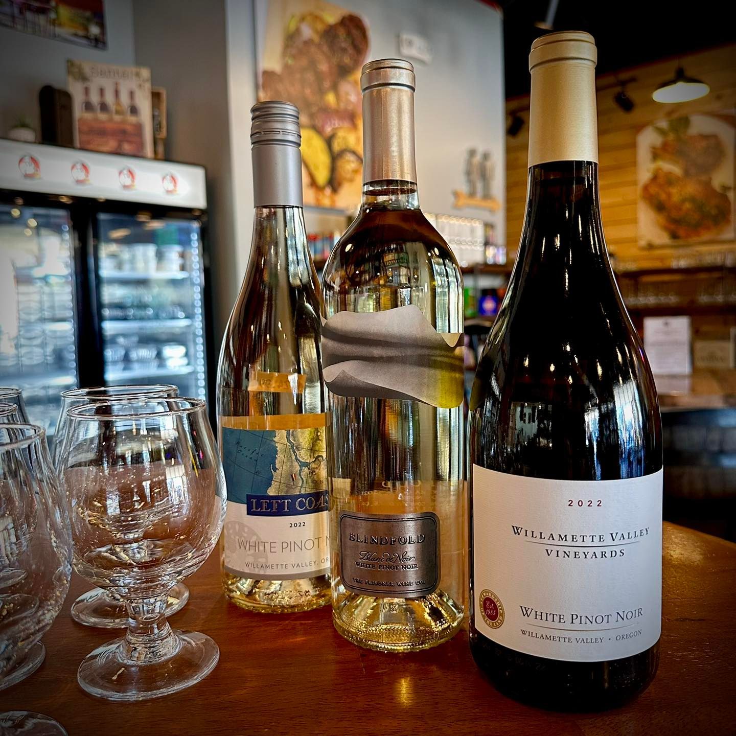 Three wine bottles on a table, with several empty glasses in front. Interior shot.