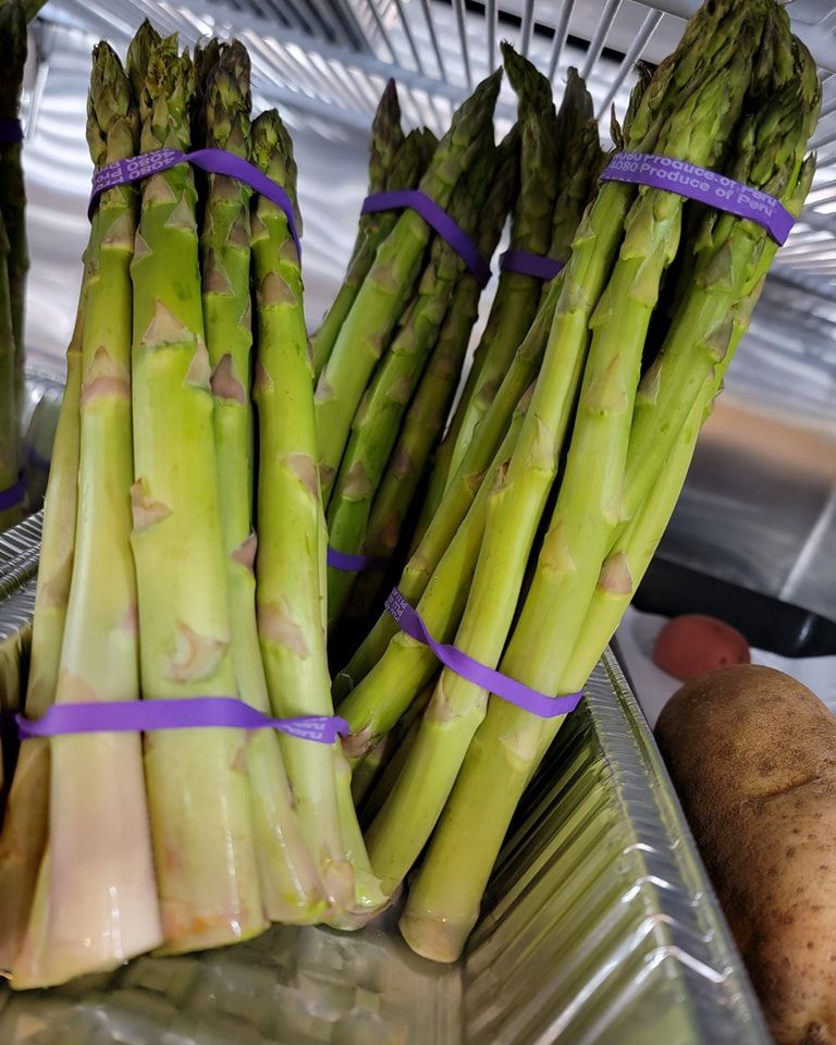 Bundles of fresh asparagus, tied with purple bands, in a metal container.