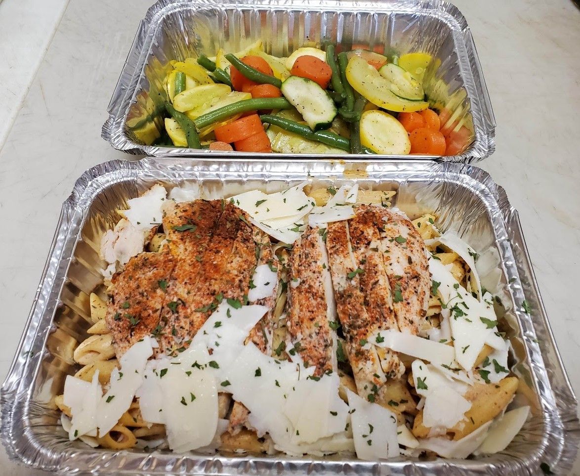 Two aluminum containers, one with pasta and chicken, the other with vegetables.