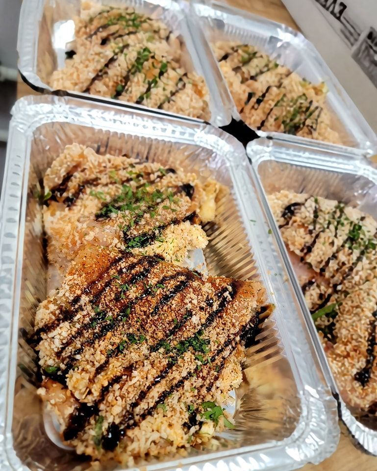 Four aluminum takeout containers holding breaded chicken, drizzled sauce, and garnish.