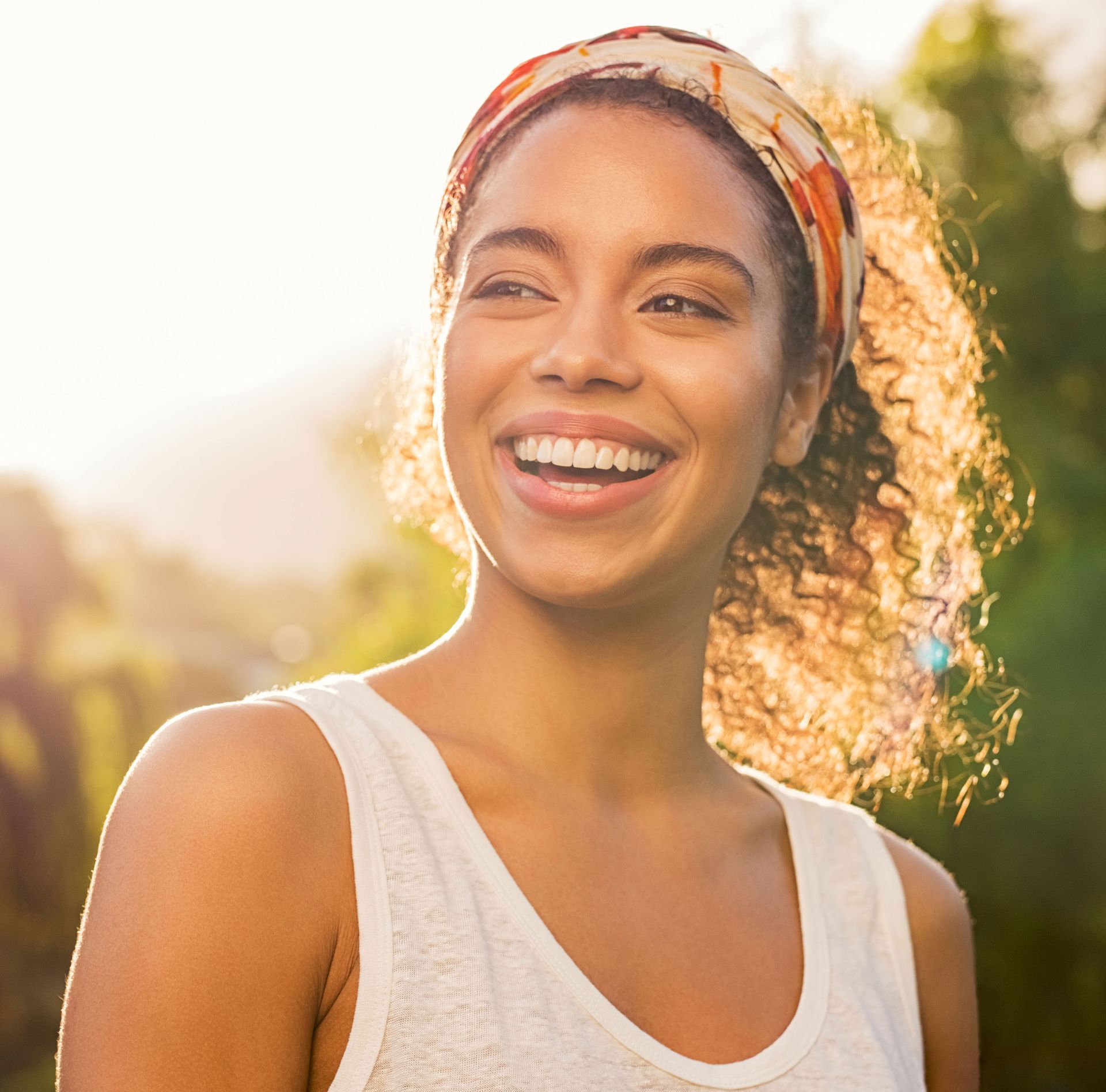 A woman wearing a headband and a white tank top is smiling.