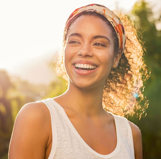 A woman wearing a headband and a white tank top is smiling.