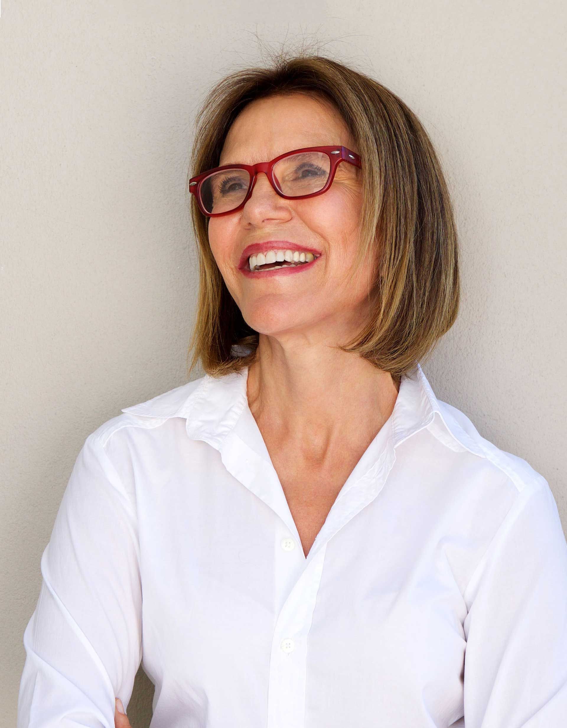 A woman wearing glasses and a white shirt is smiling.