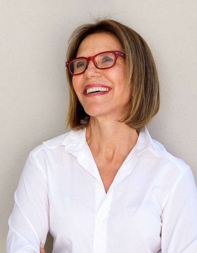 A woman wearing glasses and a white shirt is smiling.