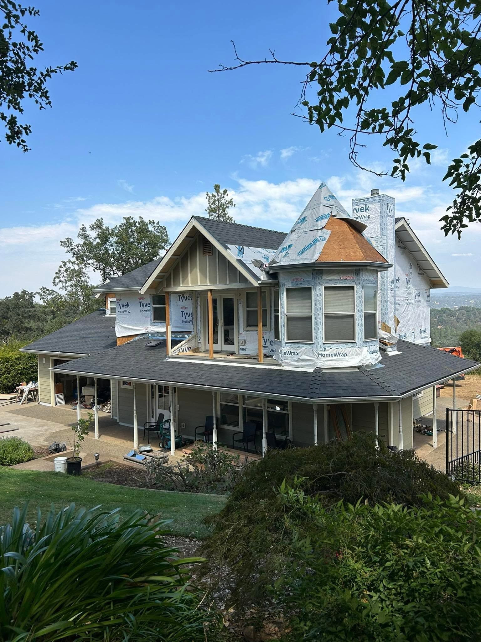 Partially renovated white house with gray roof and front porch under a blue sky