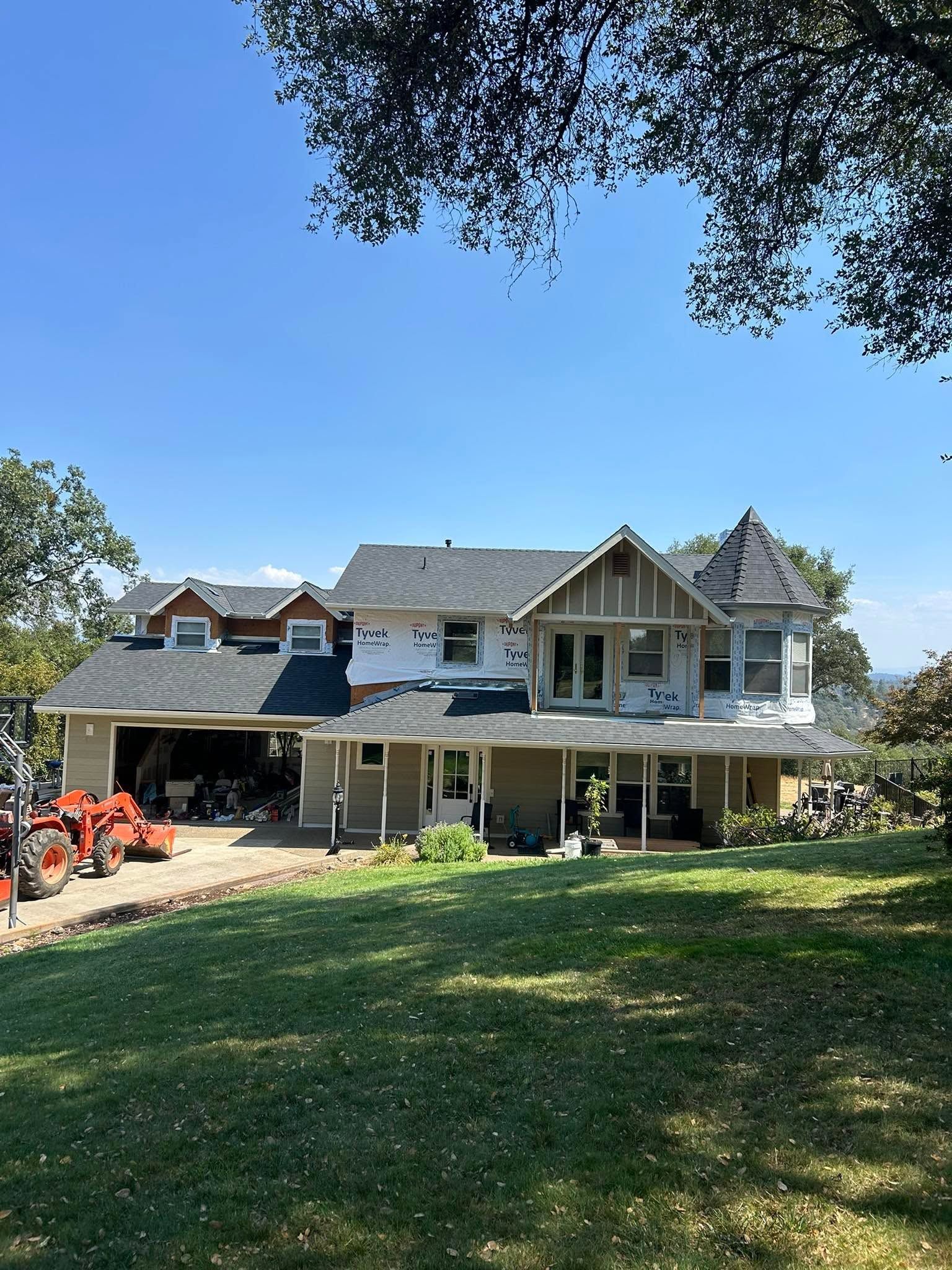Large gray house with a covered porch and dormers, viewed from a grassy yard under a clear blue sky.