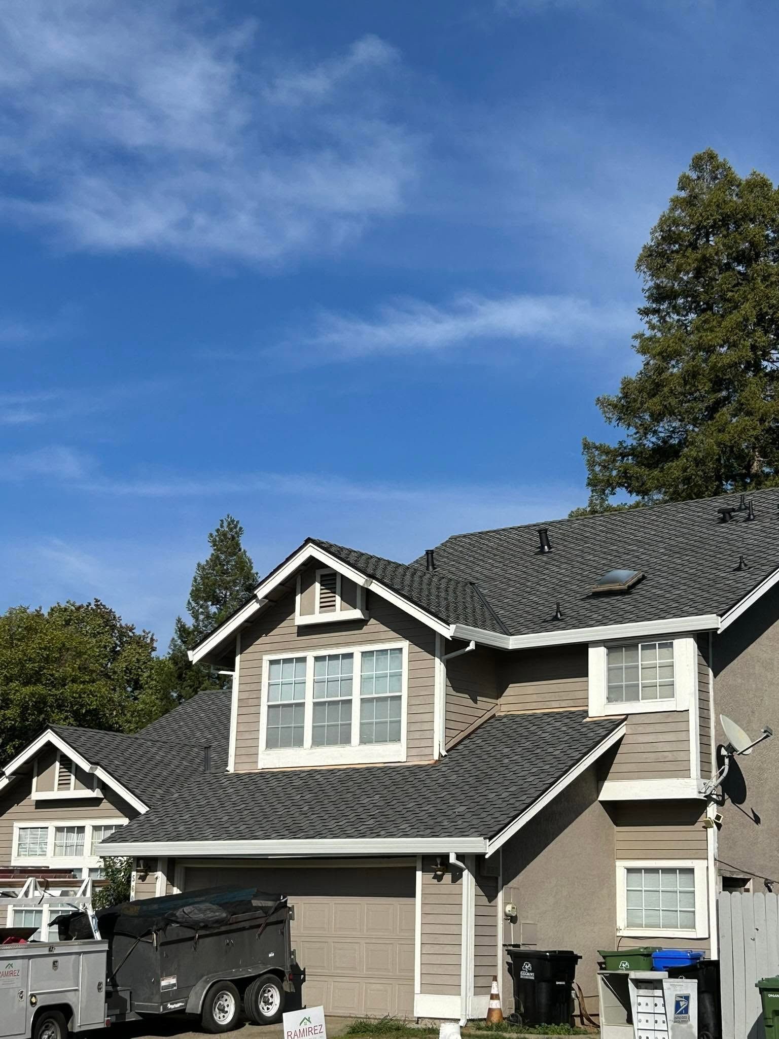 Suburban house with gray roof, parked pickup truck, and blue sky with trees around it