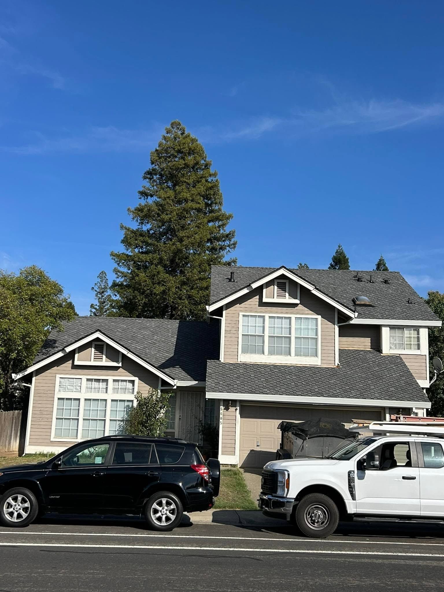 Suburban two-story house with dark roof and parked black SUV and white pickup under a bright blue sky