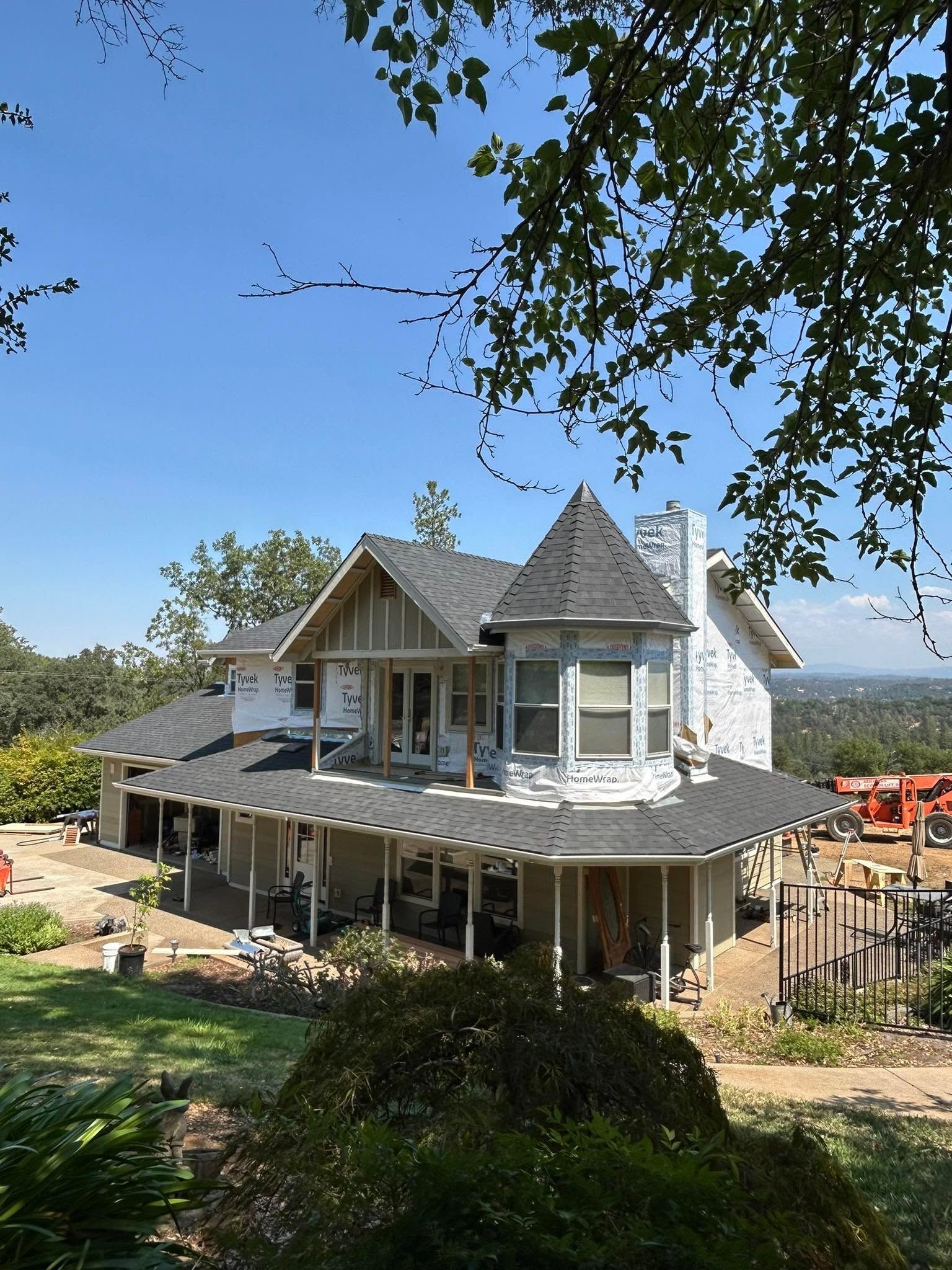 Two-story house under construction with gray roof, white siding, and scaffolding in a wooded yard