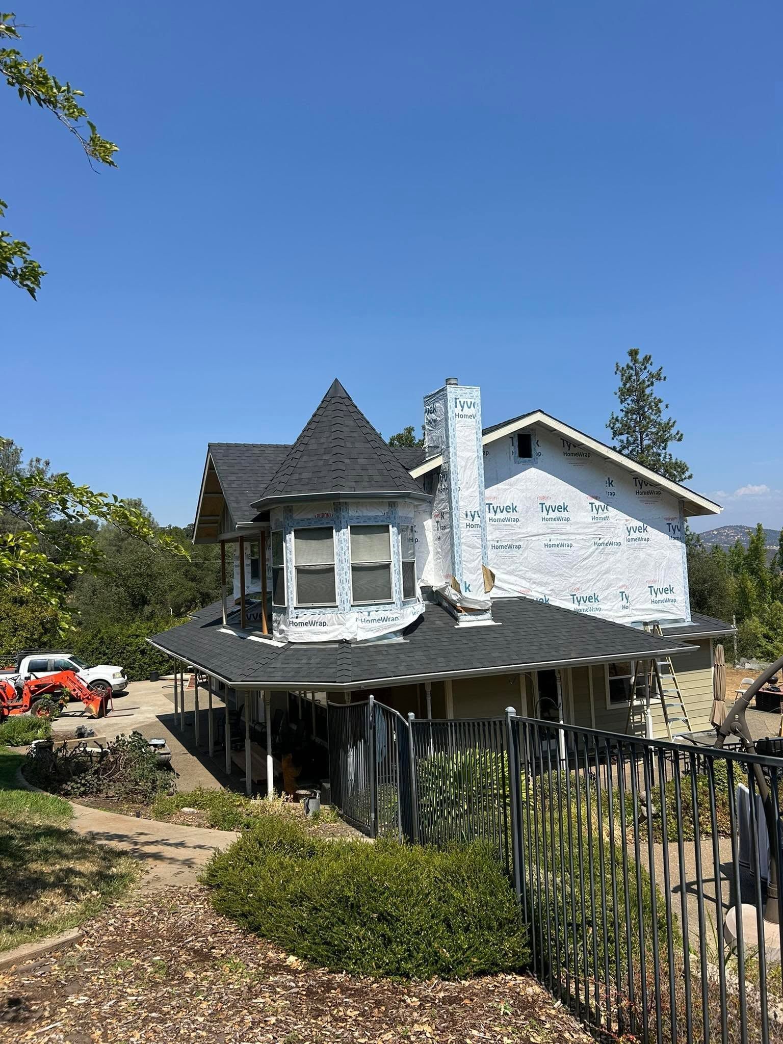 Two-story white house with dark roof and porch, viewed from a garden behind a black fence under a blue sky