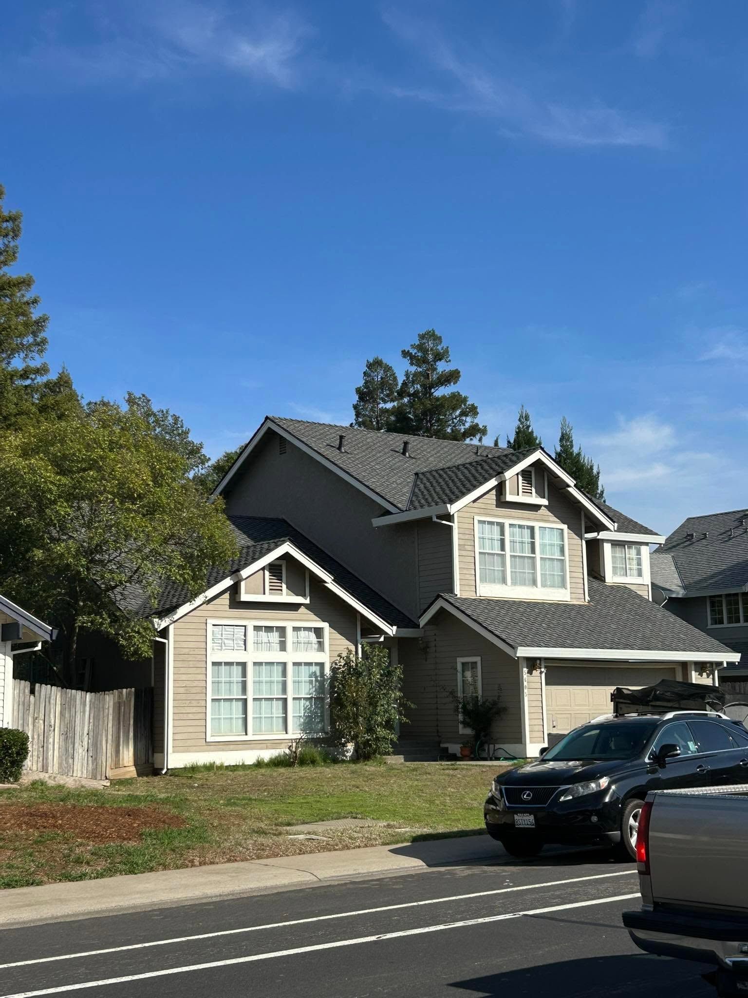 Suburban house with gray siding and white trim, blue sky above, and parked cars along the street.