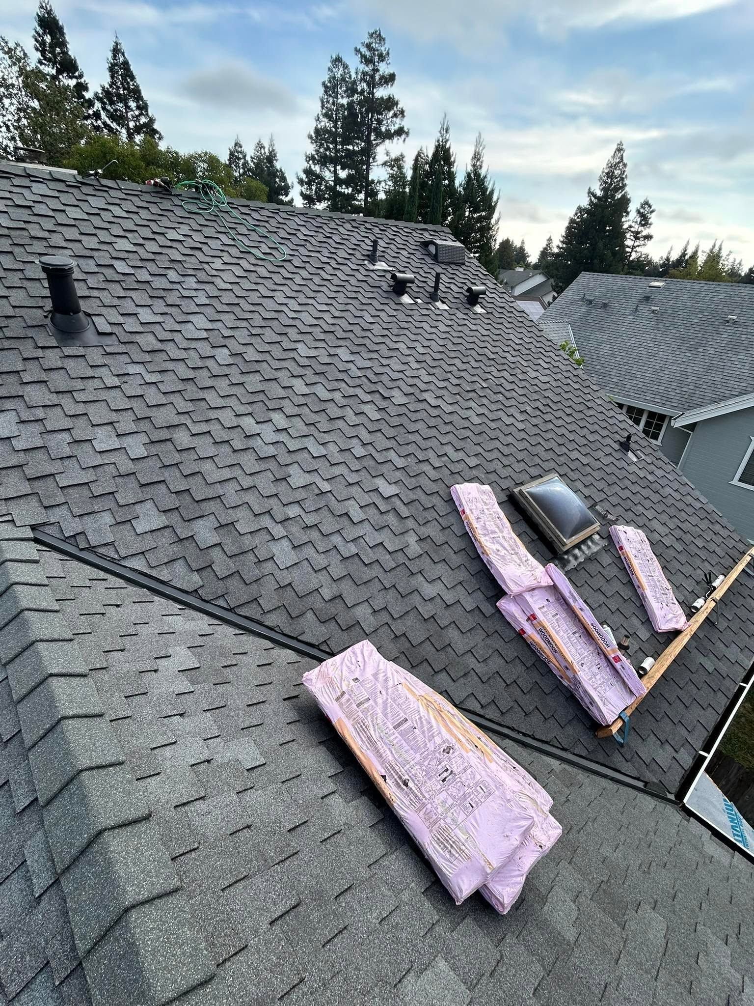 Partially repaired shingle roof with pink insulation boards and a vent under a cloudy sky