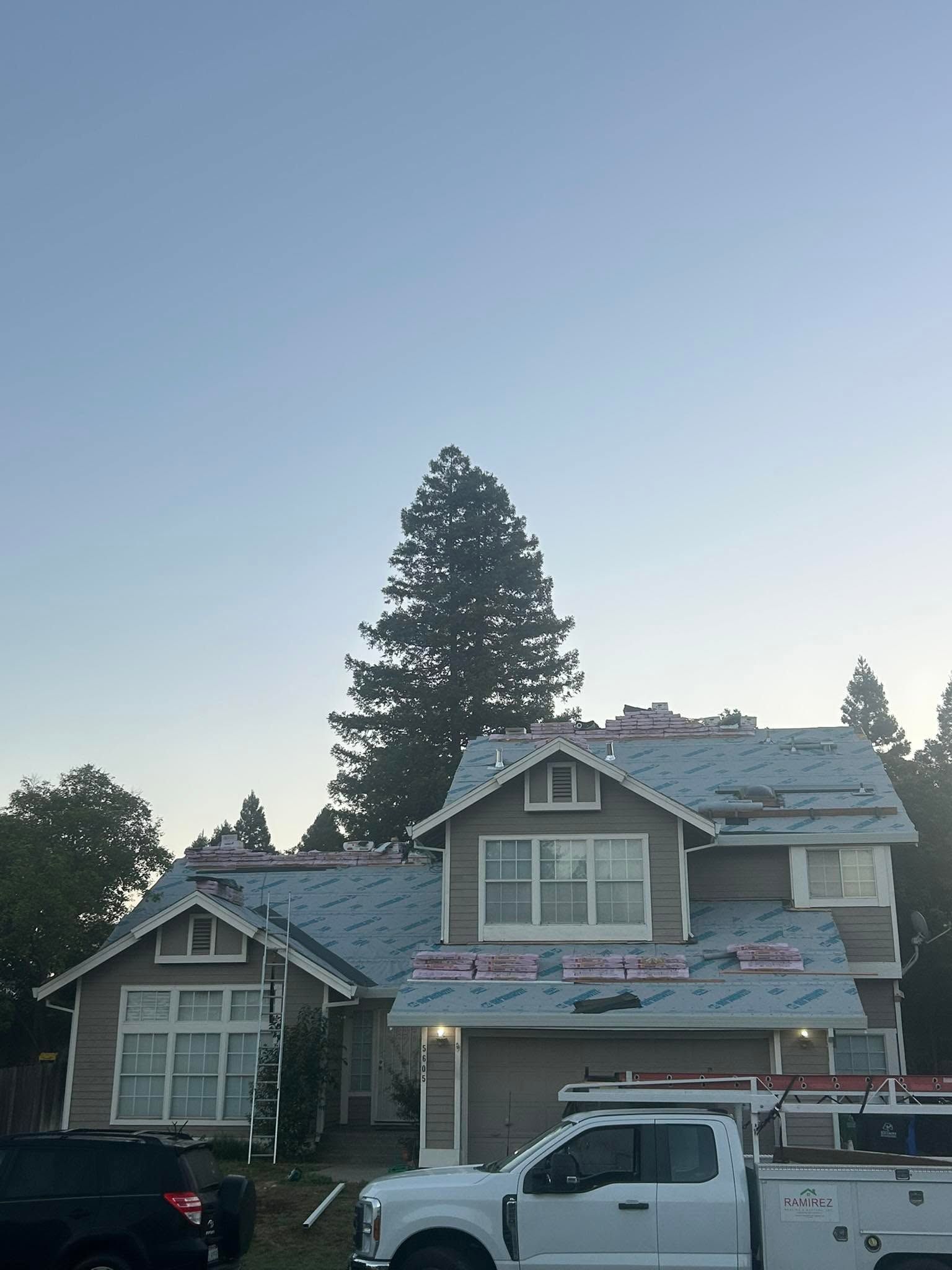 Two-story house under construction with roof scaffolding and a white pickup truck in front at dusk