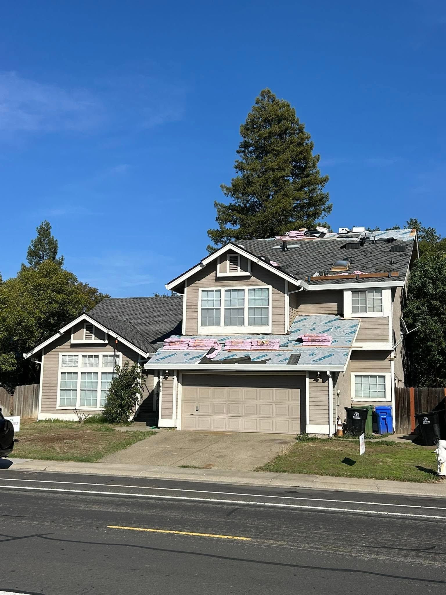 Two-story suburban house with a damaged roof and boarded garage under a clear blue sky
