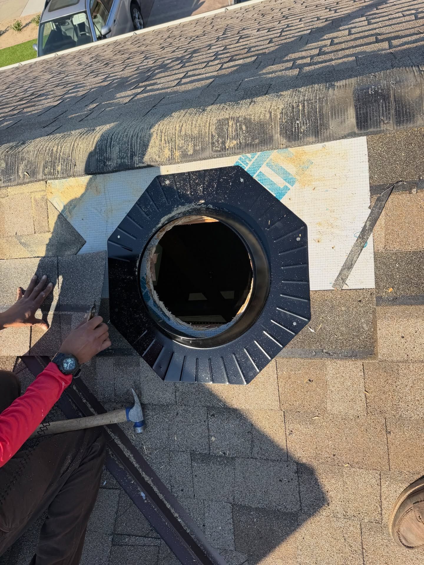 Hands working on a roof around a black octagonal vent opening and nearby tools.