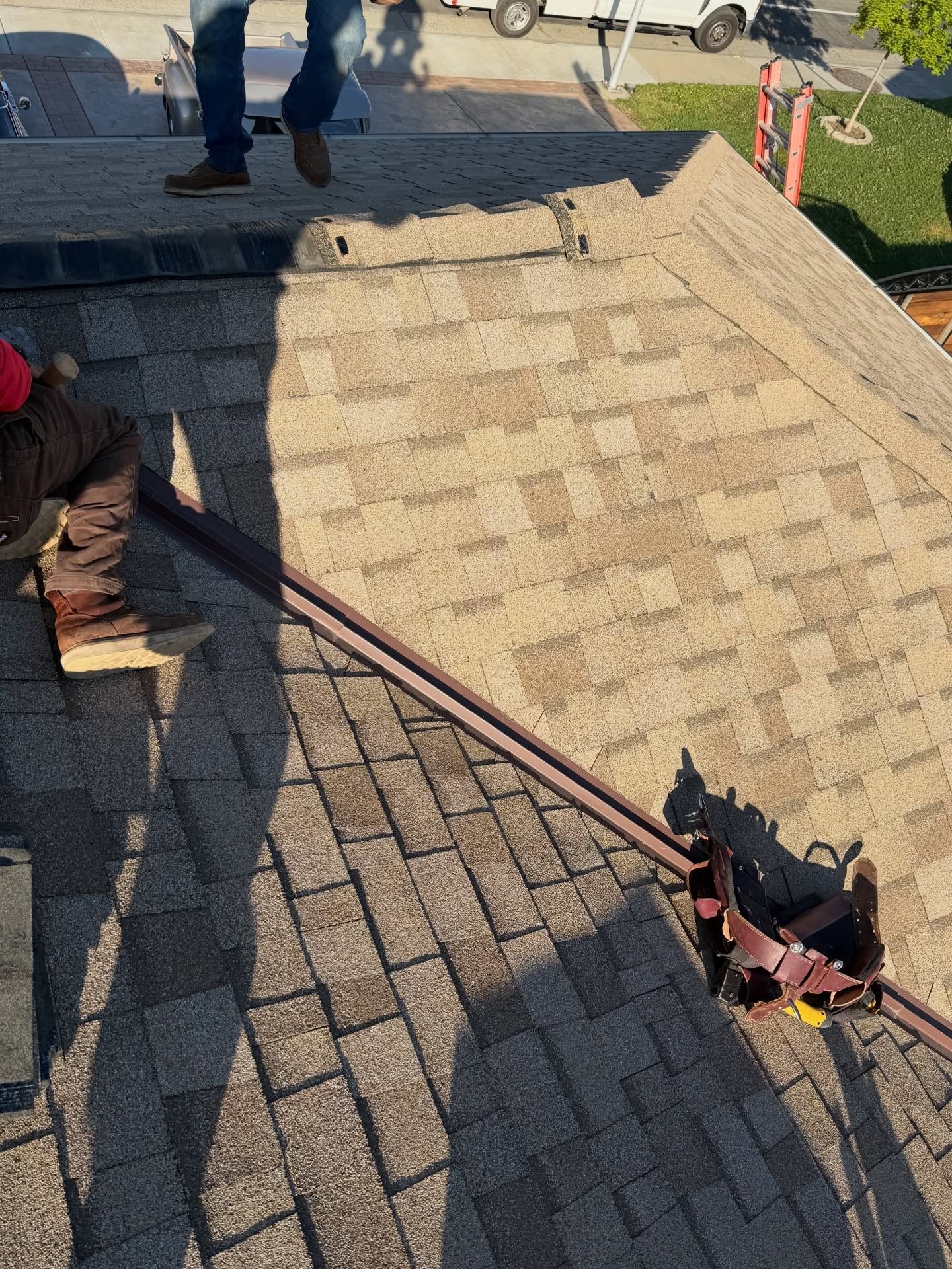Worker installing shingles on a steep roof with a nail gun and long roofing board
