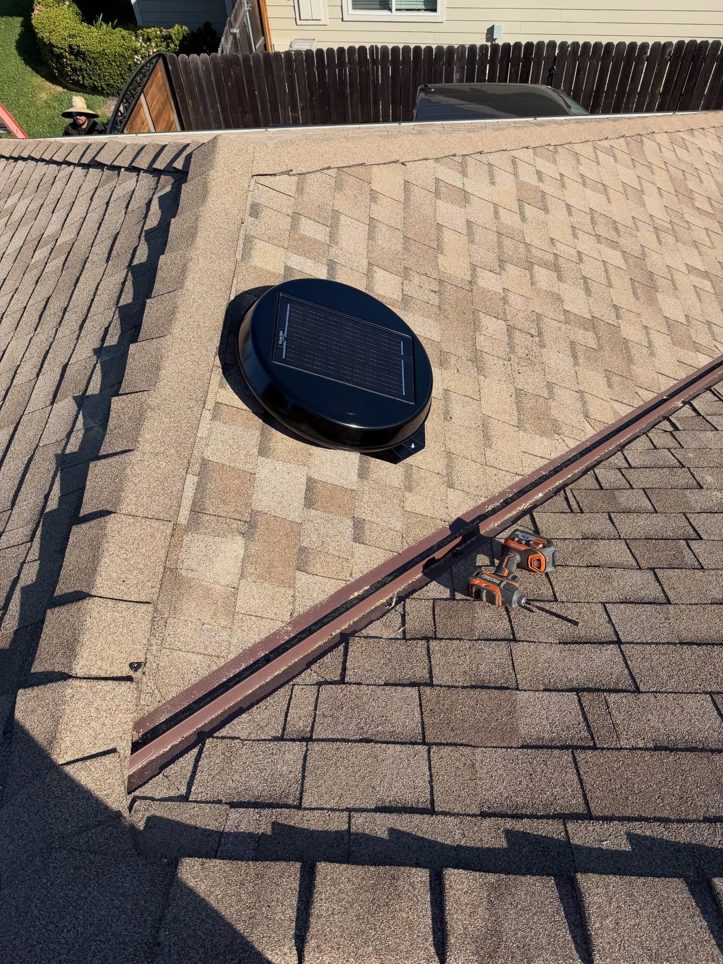 Rooftop with beige shingles, a black vent, and a roof edge with visible orange hardware.