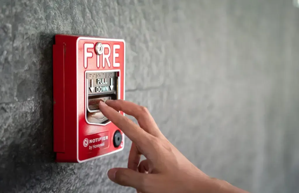 A person is pressing a button on a fire alarm.