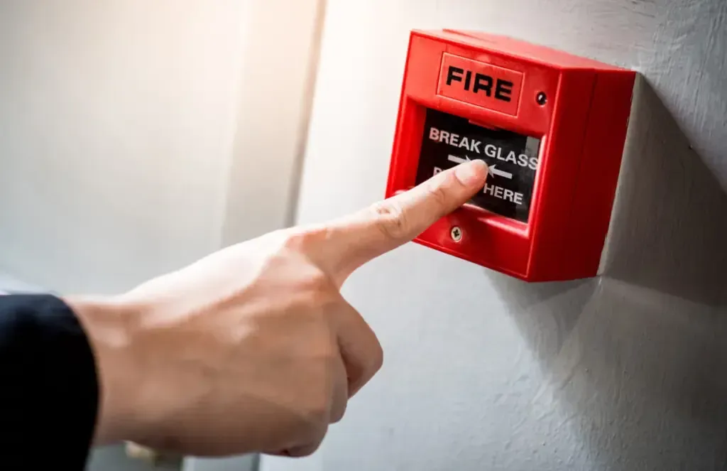A person is pressing a fire alarm button with their finger.