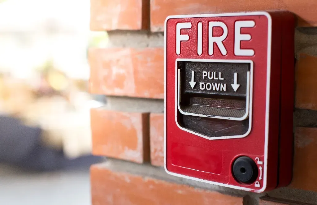 A red fire alarm is mounted on a brick wall.