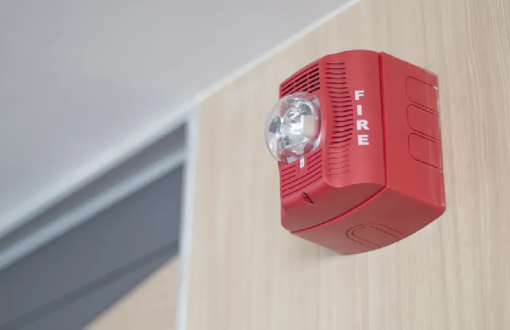 A red fire alarm is mounted on a wooden wall.