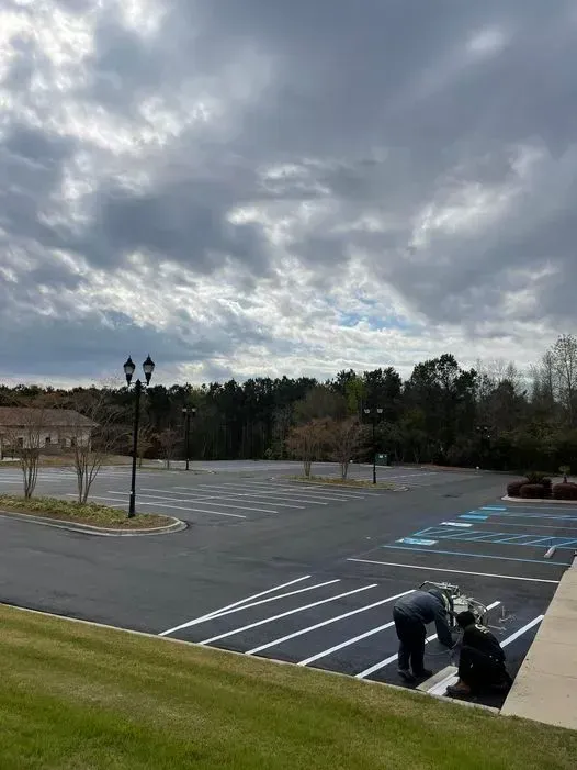 Empty parking lot under cloudy sky, with two workers painting lines near the foreground.