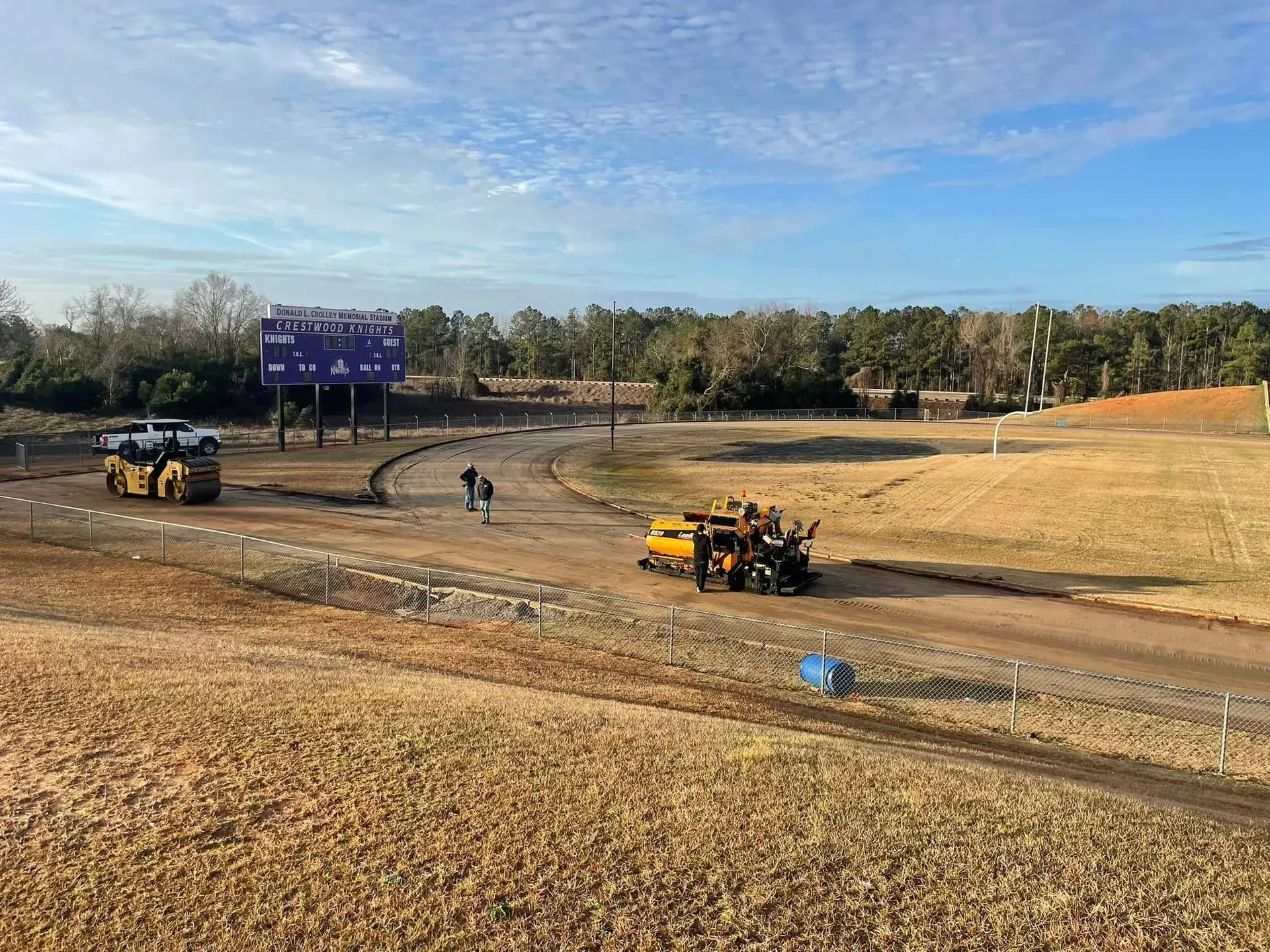 Construction vehicles grading a dirt field near a blue sign under a clear sky