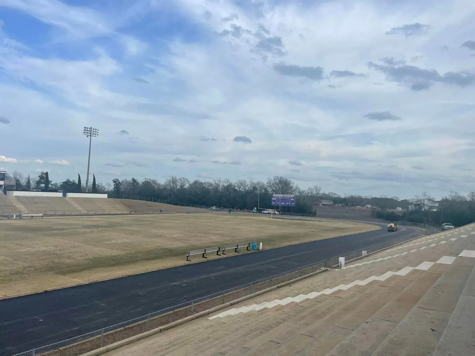 Wide outdoor race track with black lanes, grassy embankments, and a cloudy sky.