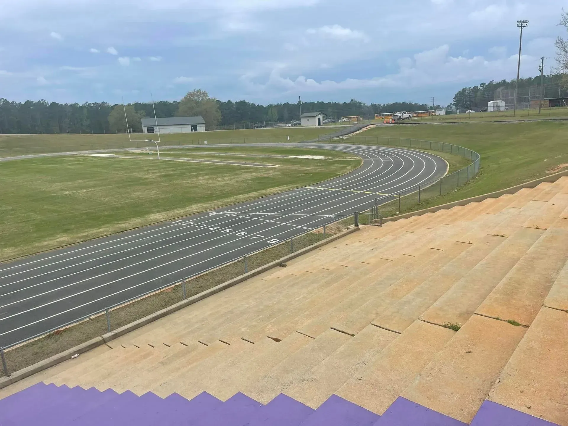 Curved race track with painted lanes beside a grassy field under a cloudy sky