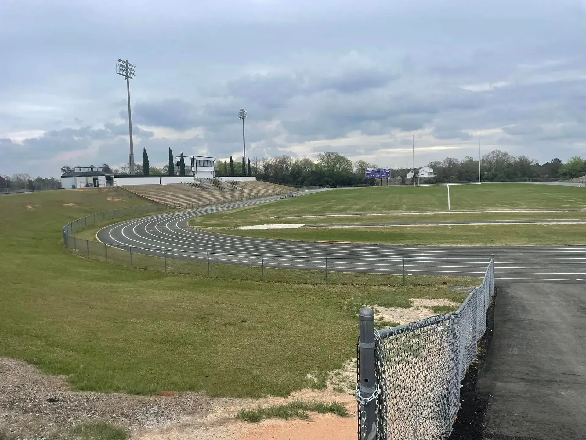 Grassy racetrack with curved asphalt track, chain-link fence, and cloudy sky