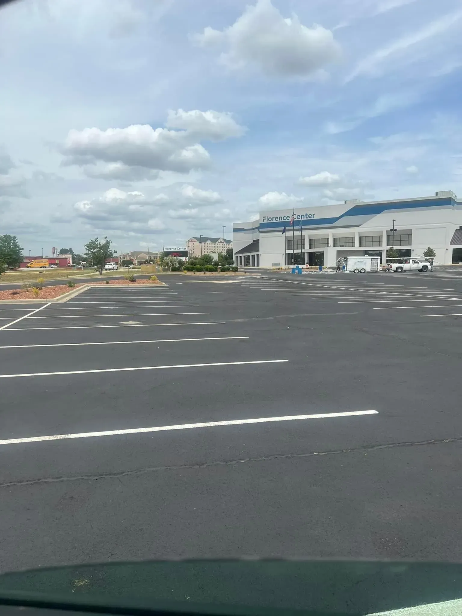 Empty parking lot beside a white commercial building under a cloudy blue sky