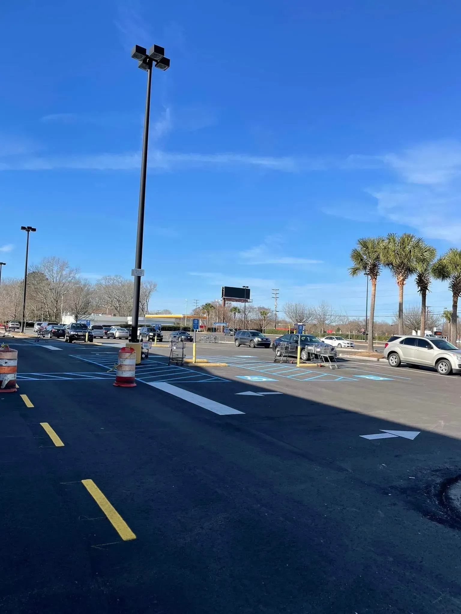Parking lot with tall light poles, cars, palm trees, and blue sky on a clear day