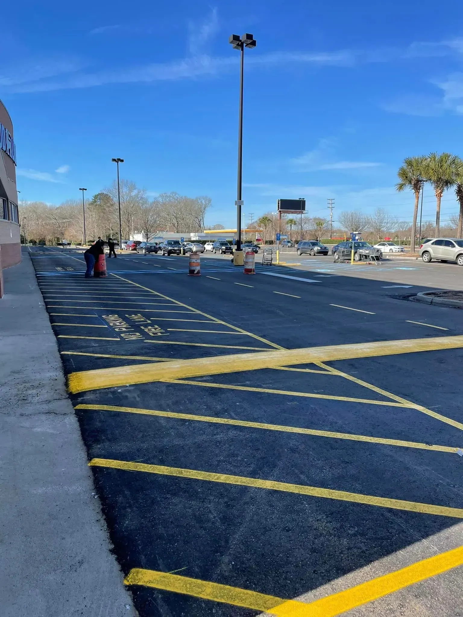Empty parking lot with yellow crosshatched no-parking markings and a few distant people under a clear sky