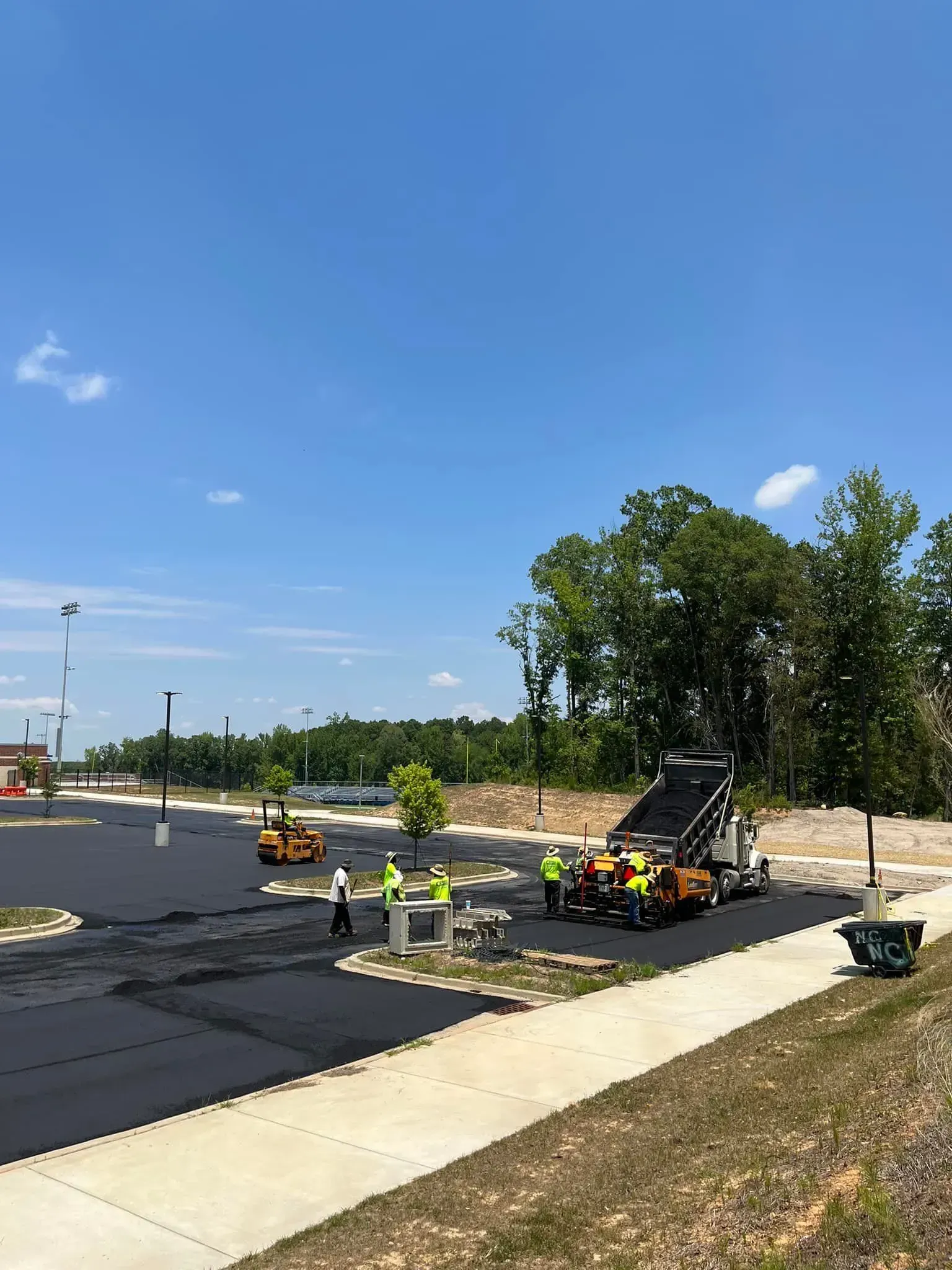 Road paving crew working on a new asphalt lot under a clear blue sky