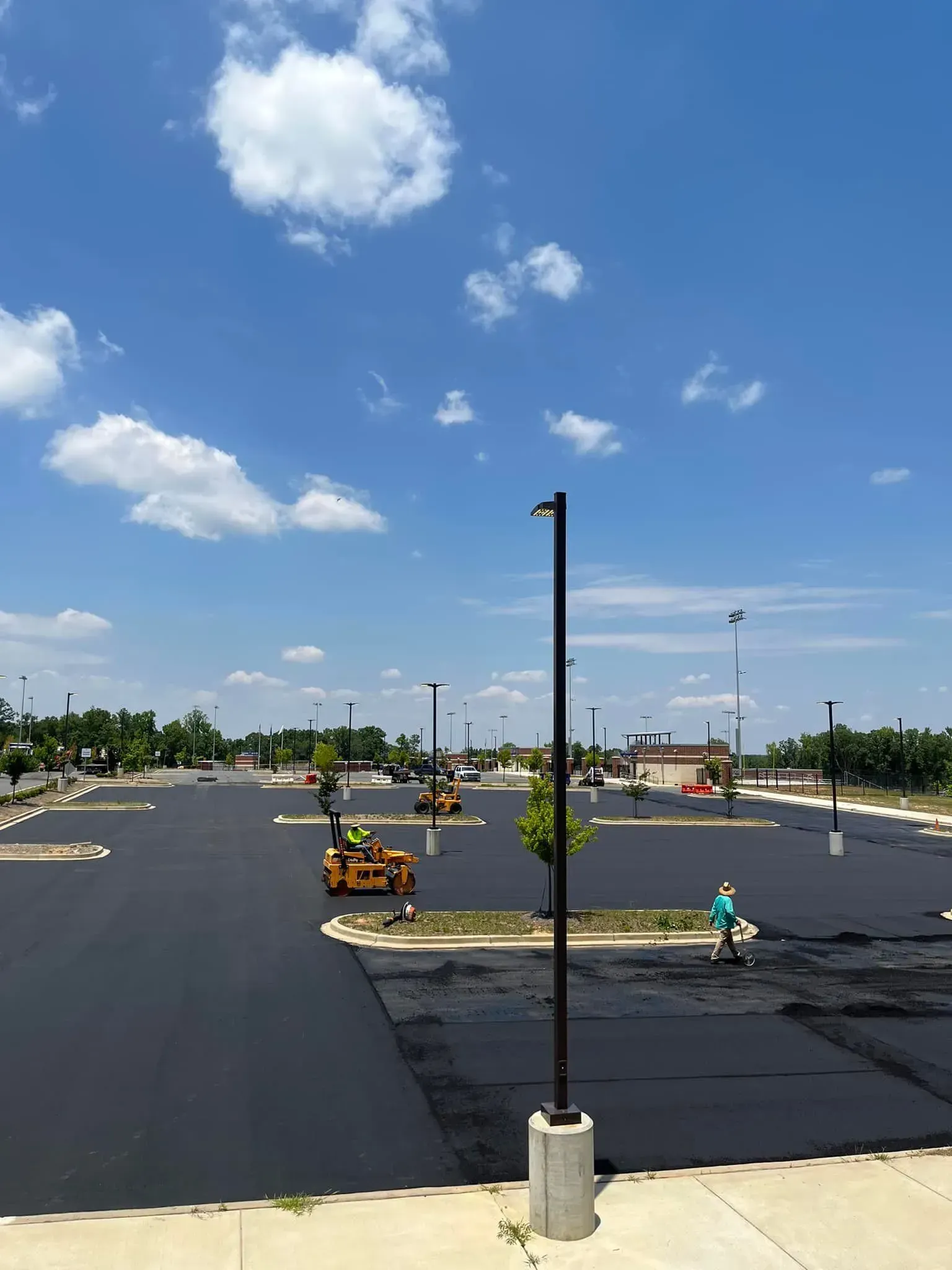 Empty parking lot under blue sky, with new asphalt, light poles, and small landscaping islands.