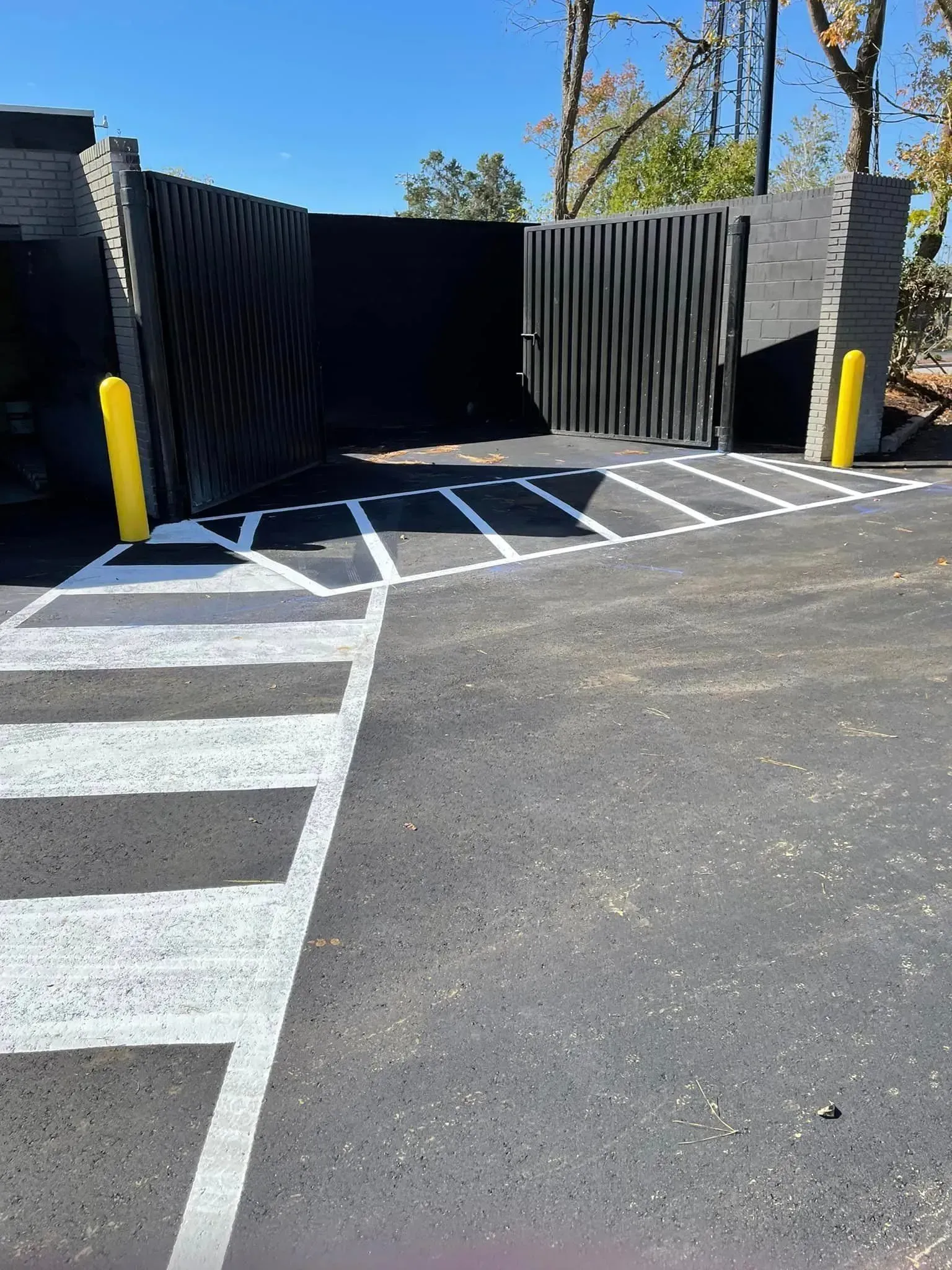 Parking lot entrance with black gate, yellow bollards, and white striped crosswalk markings