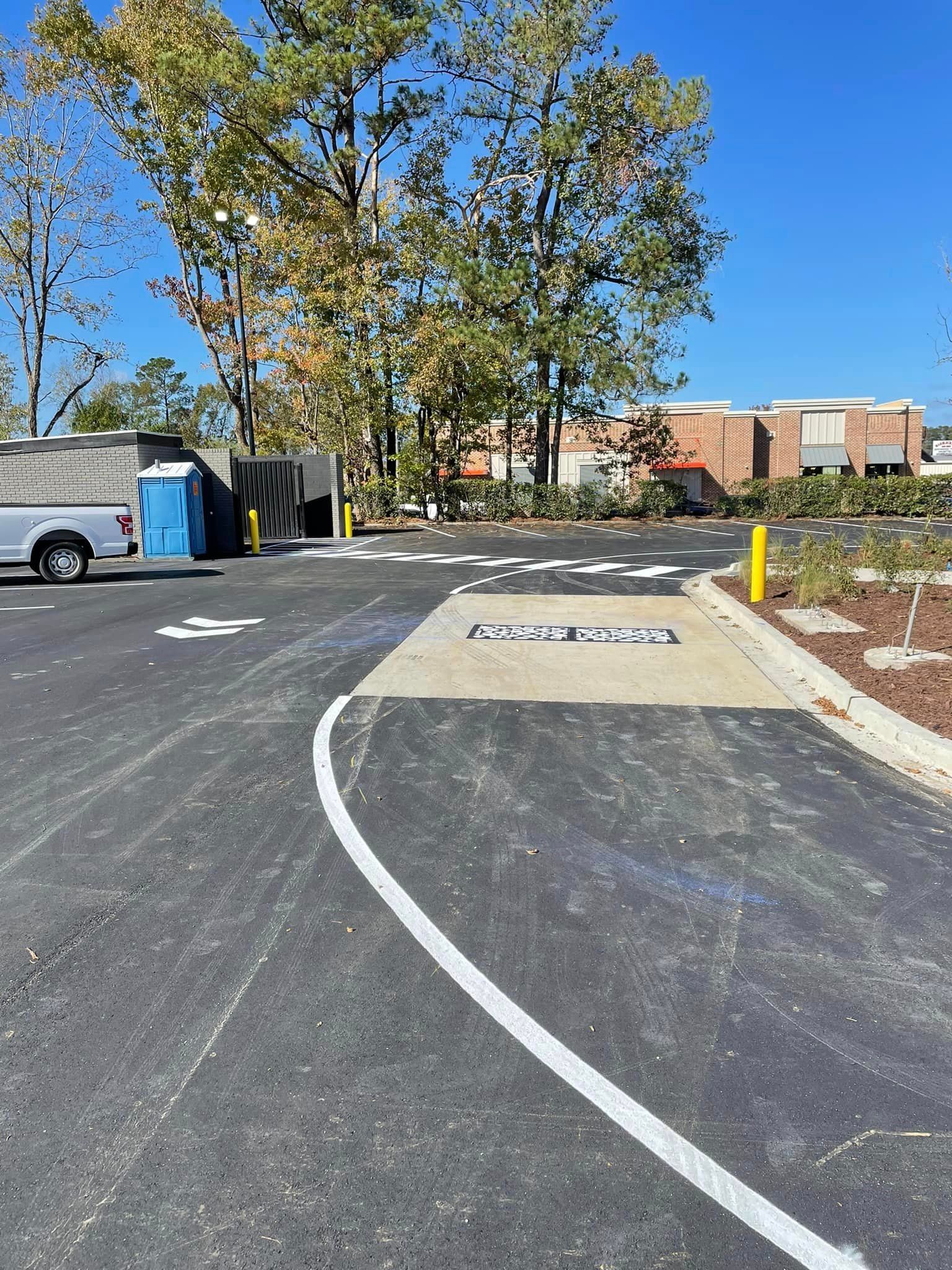 Parking lot lane with a white curb ramp, curved road markings, trees, and a brick building in the background