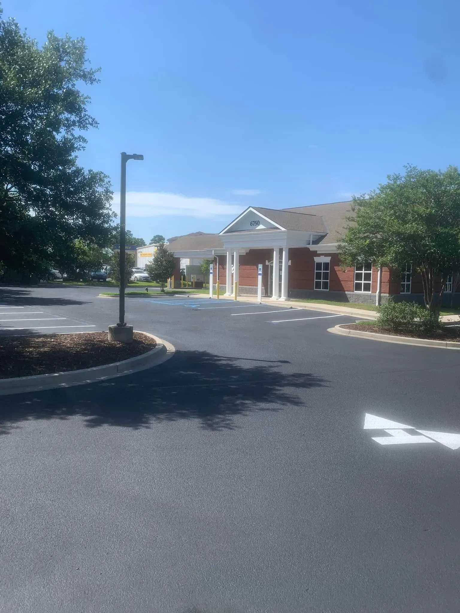Brick building entrance with white columns, surrounded by a paved driveway and trees under a clear blue sky