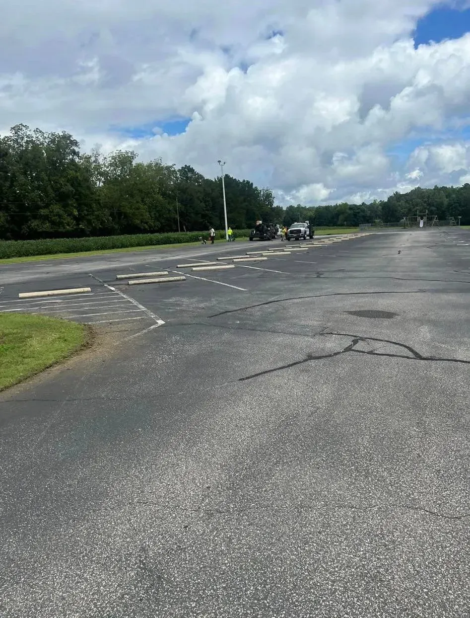 Empty parking lot with cracked asphalt, trees, and cloudy sky