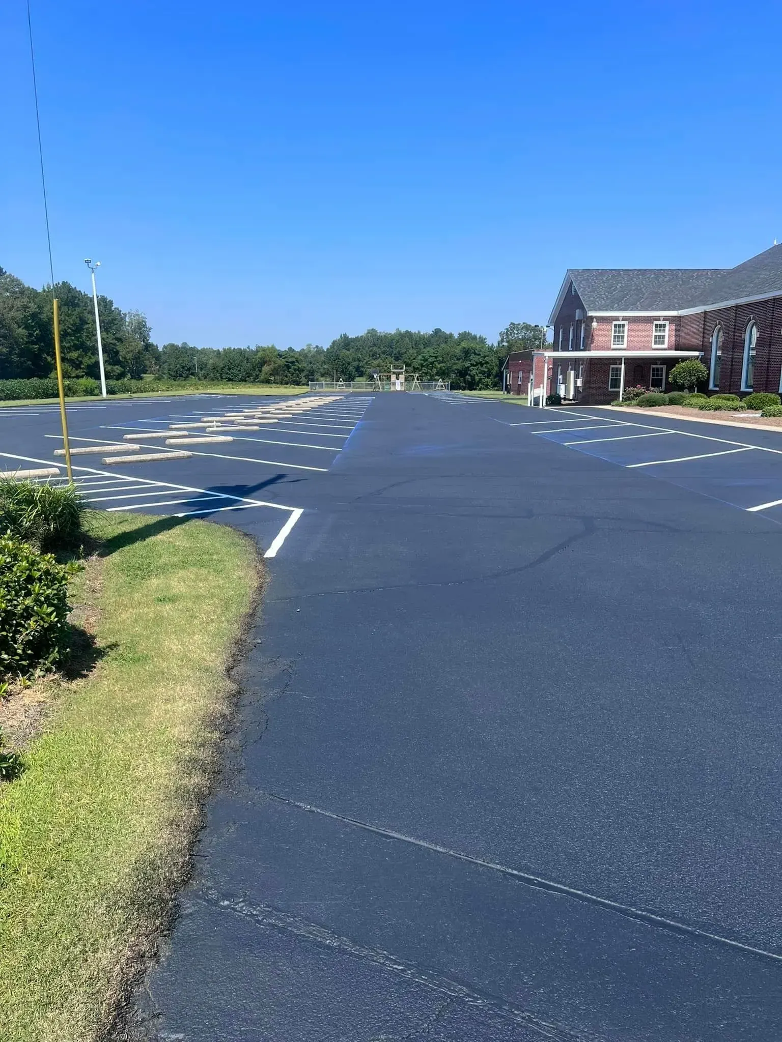 Empty asphalt parking lot with yellow markings beside a brick building on a sunny day
