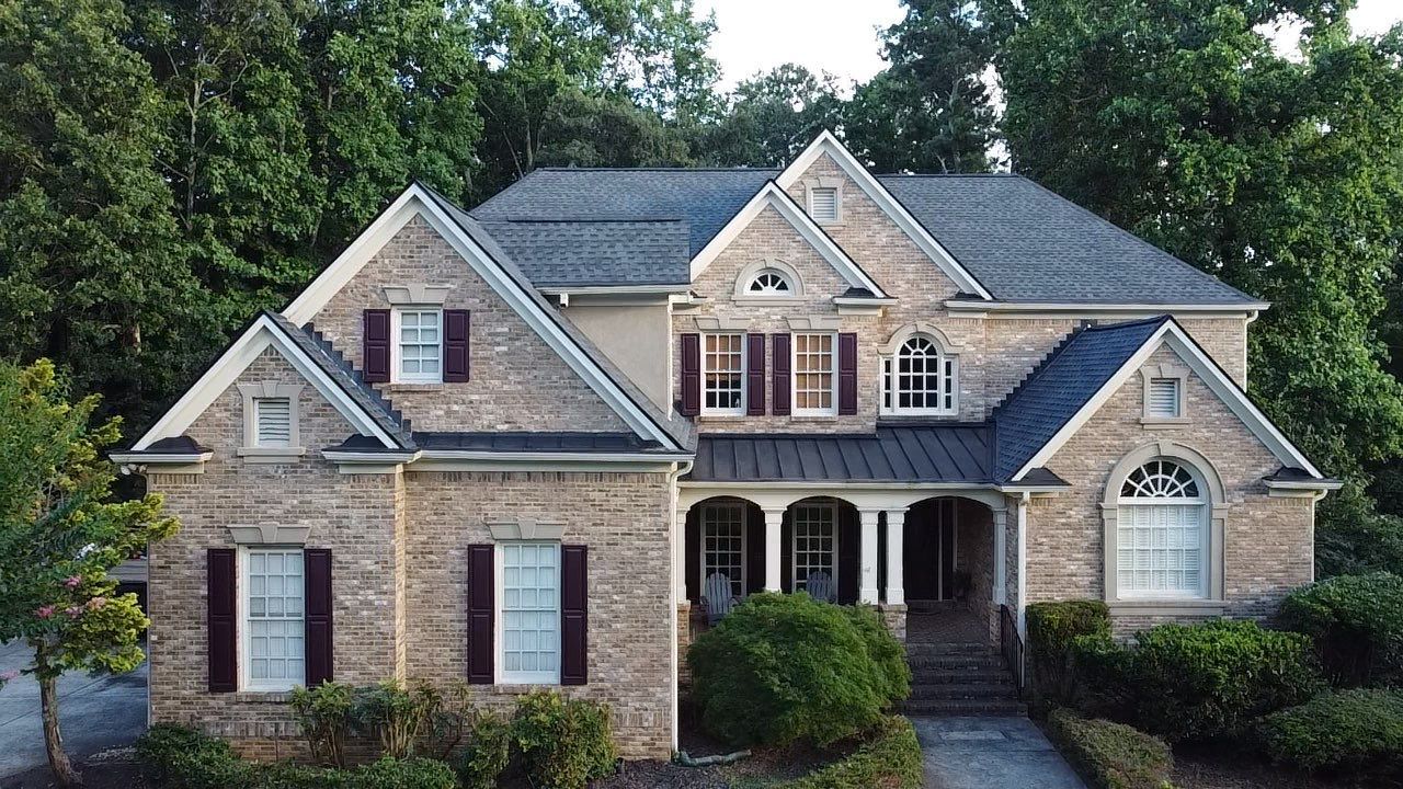 Two-story brick house with a dark gray roof, red shutters, and a covered porch.