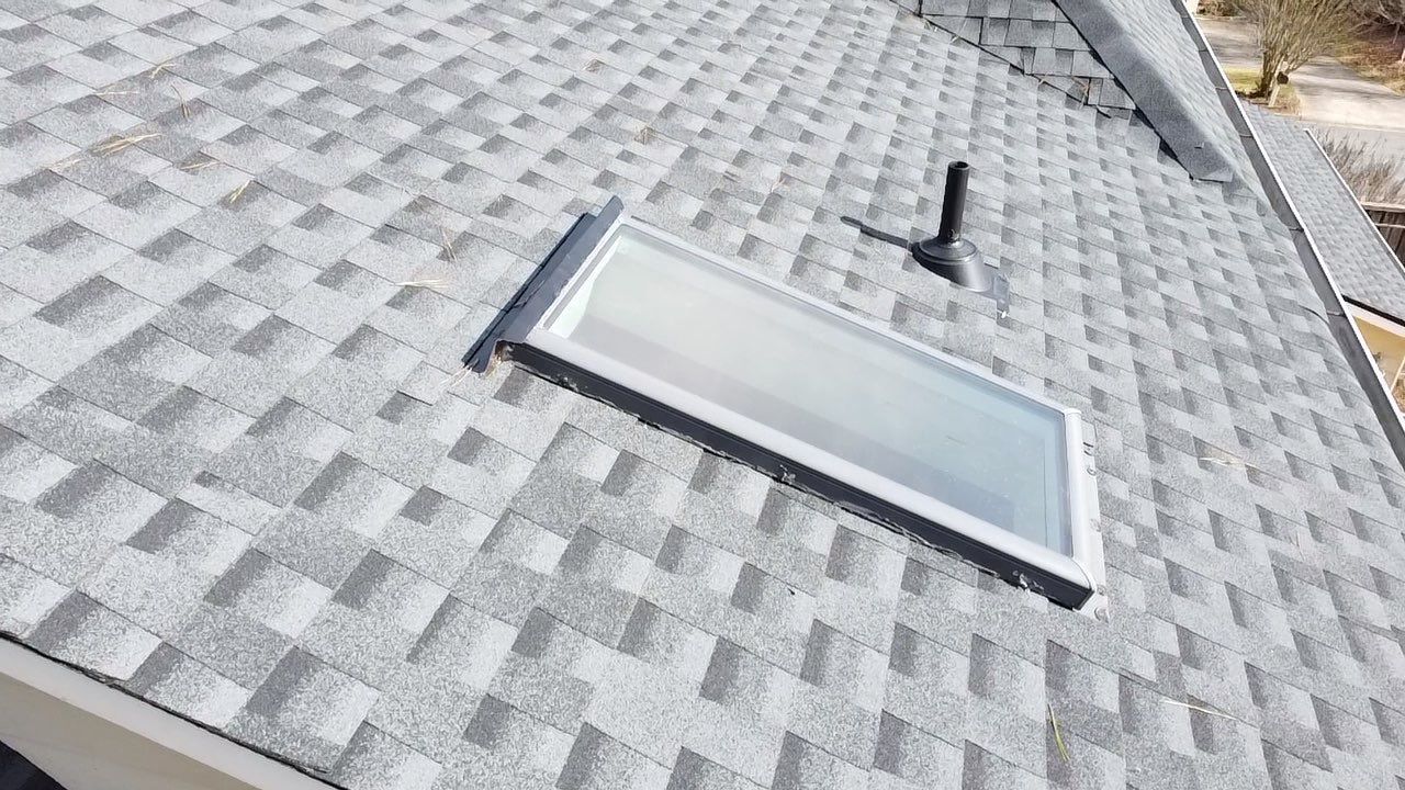 Skylight on a gray shingled roof with a black vent pipe and a gutter visible.